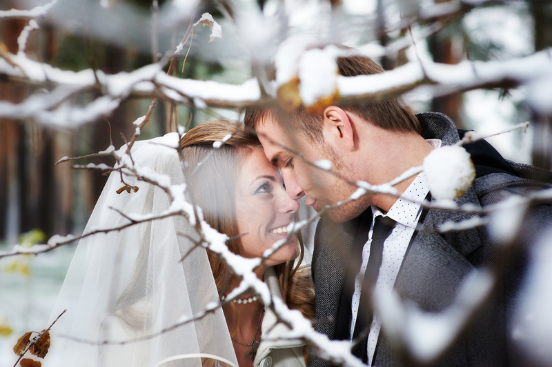 Die Winterhochzeit - Küssendes Brautpaar inmitten schneebedeckter Bäume