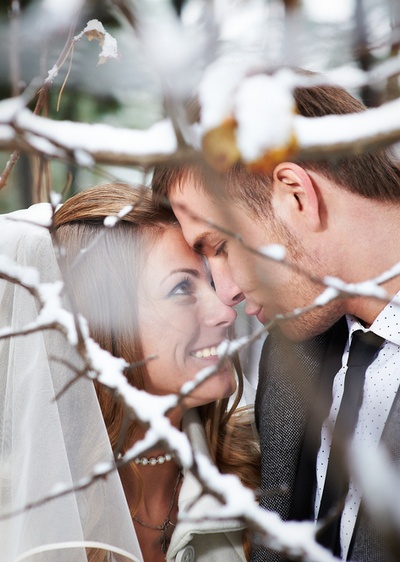 Die Winterhochzeit - Küssendes Brautpaar inmitten schneebedeckter Bäume