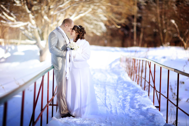 Die Winterhochzeit - Küssendes Brautpaar auf verschneiter Brücke